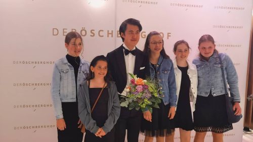 Pianist Haiou Zhang hält einen Blumenstrauß und posiert mit jungen Fans