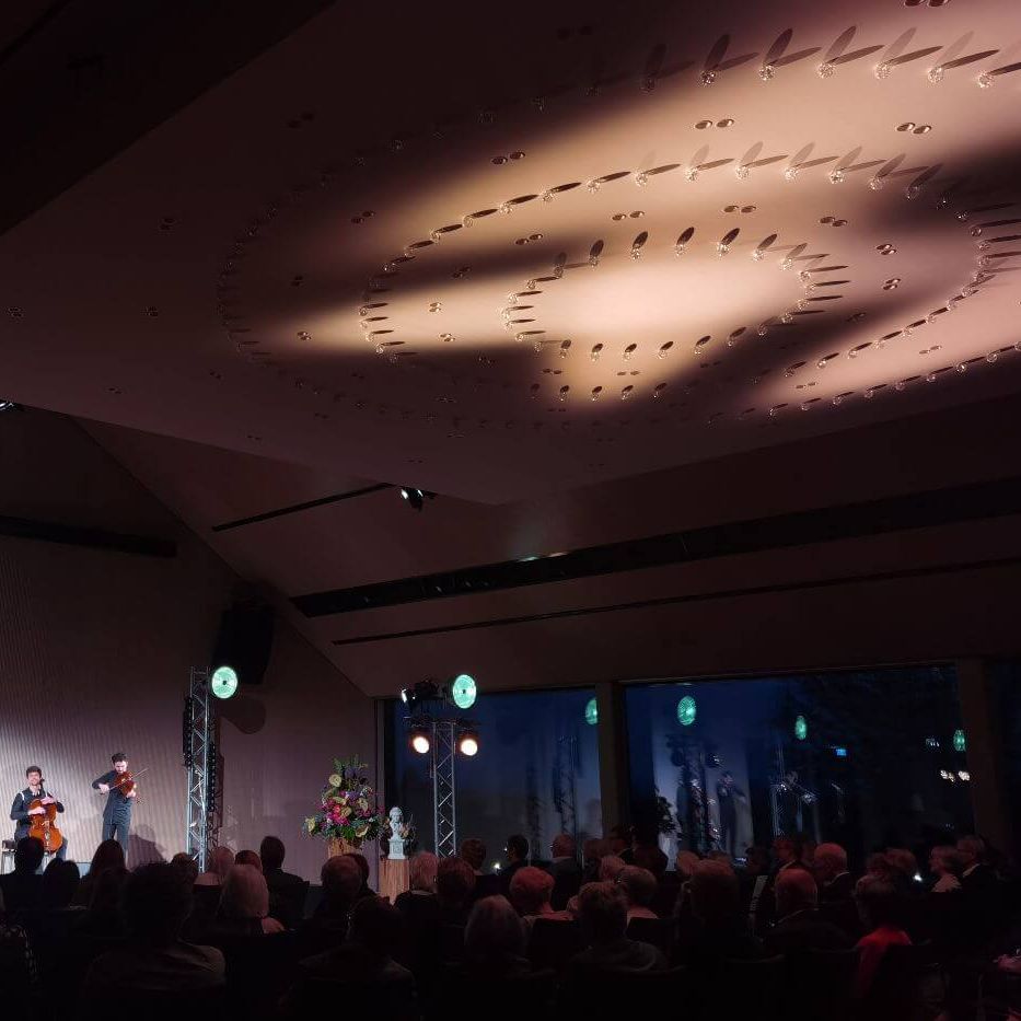 Two string players perform a concert on an illuminated stage