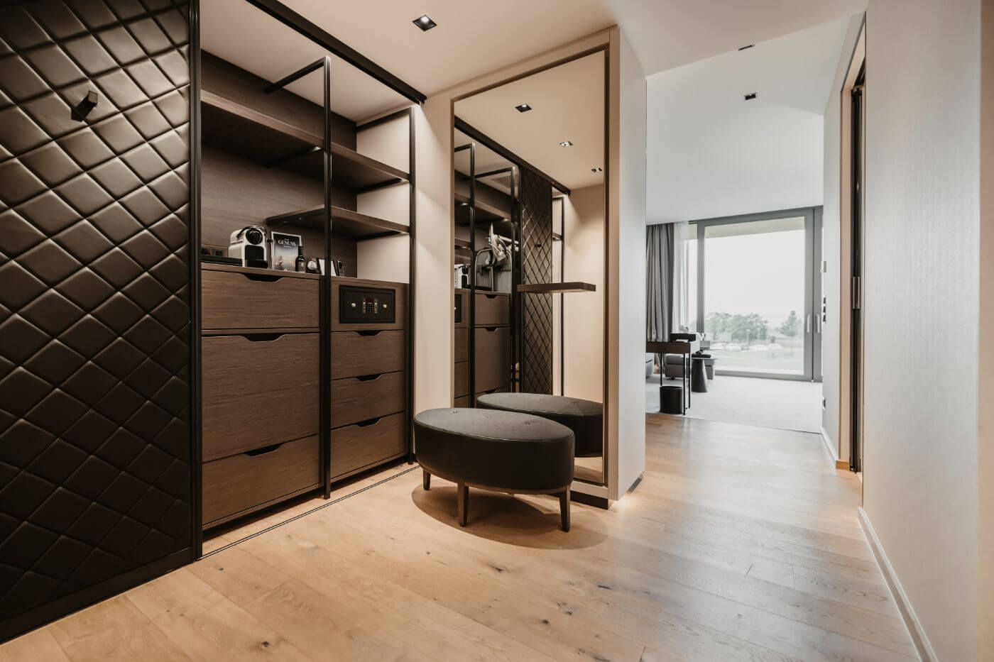 Dark wood closet equipped with a coffee machine next to an armchair by a floor-to-ceiling mirror